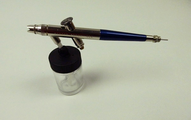 Image of an airbrush with paint reservoir, as part of a guide blog about model airbrush techniques.